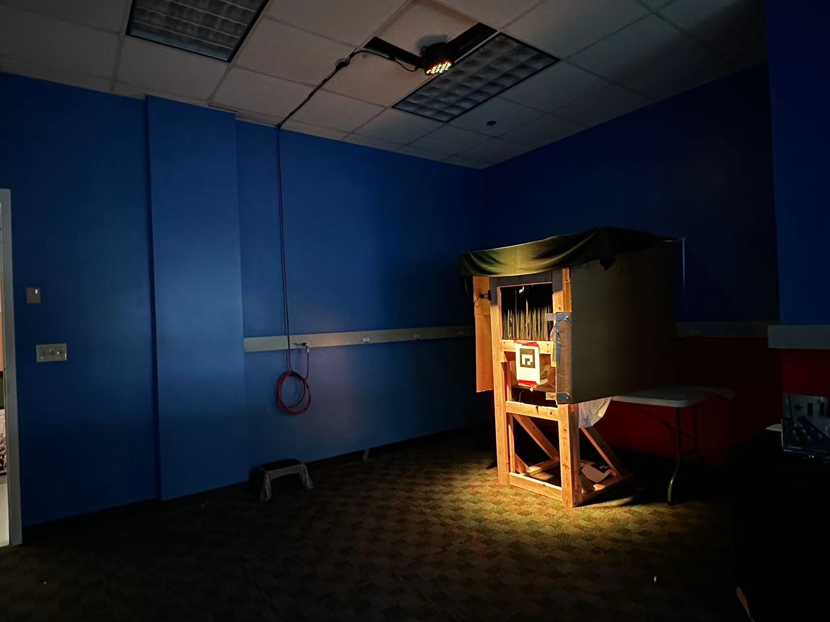 The physical painting frame: a wooden frame with an ArUco marker, strips of spandex where the guest looks through the painting, and a box covering a shelf that the guest looks into